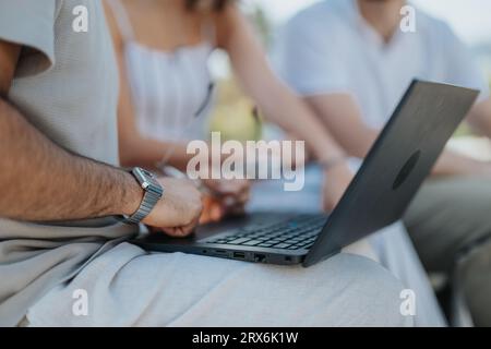 Eine Gruppe von Architekten und Designern arbeitet im Freien zusammen und diskutiert Blaupausen auf einem Tablet und Laptop. Sie arbeiten zusammen, um einen erfolgreichen Buil zu schaffen Stockfoto