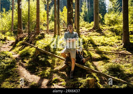 Mann mit gekreuzten Armen, der sich im Wald an einem Baum lehnt Stockfoto