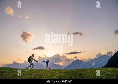 Mädchen, das auf den Vater zuläuft, der auf einer Wiese am Berg steht Stockfoto