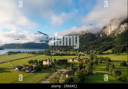 Österreich, Oberösterreich, Sankt Lorenz, Dröhnblick auf Nebelsammeln über einem kleinen Dorf mit Bergen im Hintergrund Stockfoto