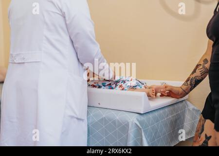 Ein Arzt untersucht ein Baby in einer Arztpraxis und stellt mit der anwesenden Betreuungsperson Gesundheitsversorgung und Behandlung bereit. Stockfoto