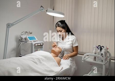 Dermatologin, die in der Klinik chemische Peelmaske auf das Gesicht der Frau aufträgt Stockfoto