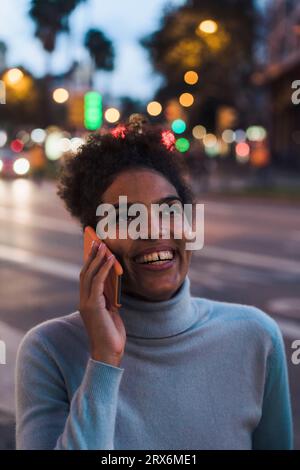 Glückliche junge Frau, die in der Abenddämmerung auf dem Smartphone spricht Stockfoto