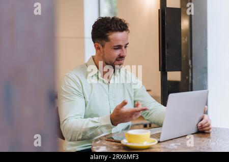 Lächelnder junger Geschäftsmann, der über einen Laptop per Videoanruf spricht Stockfoto