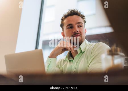 Junger Geschäftsmann mit Laptop, der im Café sitzt Stockfoto