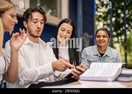 Schüler, die zusammen mit ihrem männlichen Professor Schulaufgaben lösen, versammelten sich am Tisch, draußen. Stockfoto