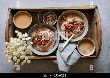 Studio-Schuss aus Holztablett mit Schüsseln aus veganem Brei, Wildblumen und Rhabarberkompott Stockfoto