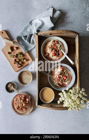 Studio-Schuss aus Holztablett mit Schüsseln aus veganem Brei, Wildblumen und Rhabarberkompott Stockfoto