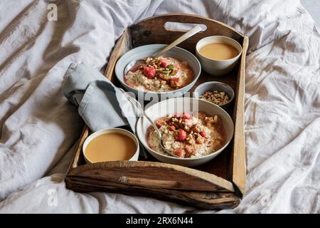 Holztablett mit Schüsseln aus veganem Brei und Rhabarberkompott auf dem Bett Stockfoto