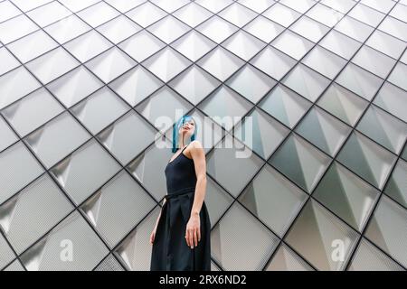 Junge Frau mit gefärbten Haaren, die vor einer gemusterten Wand steht Stockfoto