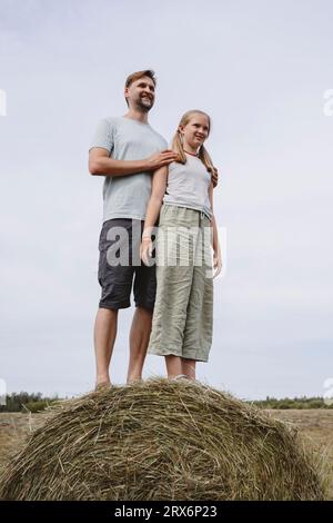 Glücklicher Vater und Tochter, die auf dem Feld auf Heu stehen Stockfoto