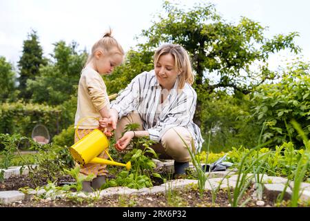 Glückliche Mutter und Tochter, die Pflanzen mit Dose im Garten tränken Stockfoto