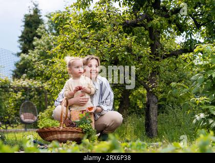 Glückliche Mutter und Tochter mit Korb mit frischem Gemüse im Garten Stockfoto