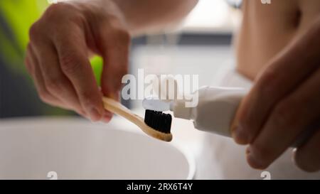 Nahaufnahme männliche Hände nicht erkennbarer Mann Mann Mann Squeeze medizinische Whitening Zahnpasta auf ECO Bambus Zahnbürste Vorbereitung der Zähne Zähneputzen Zahnreinigung Stockfoto