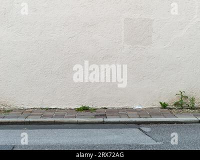 Leere weiße Wand als abstrakter Hintergrund. Die Textur eines echten Außenputzes eines Gebäudes. Die Asphaltstraße und der Bürgersteig sind ebenfalls leer. Stockfoto