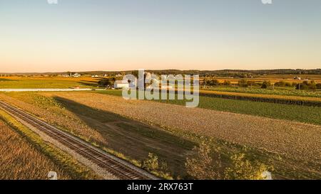 Ein Luftblick am späten Nachmittag auf Ackerland, Maisfelder, Silos, Barns und ein Single Rail Road Track, an einem späten Herbstnachmittag. Stockfoto