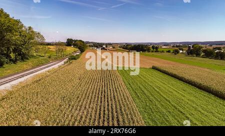 Ein Luftblick am späten Nachmittag auf Ackerland, Maisfelder, Silos, Barns und ein Single Rail Road Track, an einem späten Herbstnachmittag. Stockfoto