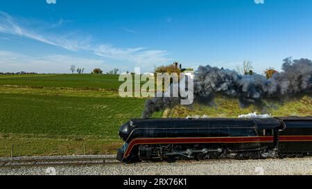 Ein Blick von der Luft auf eine antike stromlinienförmige Dampflokomotive, die durch die Blase von schwarzem Rauch fährt, durch die Landschaft an einem Herbsttag Stockfoto