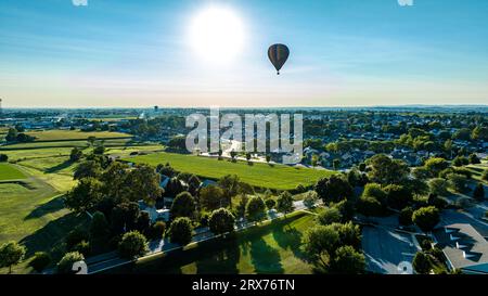 Ein Luftblick auf einem gestreiften Heißluftballon, der an einem späten Nachmittag über einer ländlichen Gemeinde schwimmt, ein wunderschöner Sommertag Stockfoto