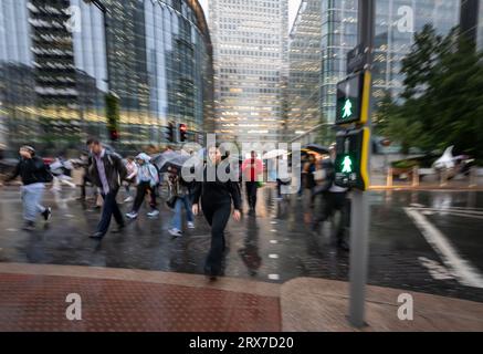 Canary Wharf, London, UK: Menschen überqueren die Straße an Ampeln in Canary Wharf mit Bewegungsunschärfe. Die Leute halten Regenschirme im Regen. Stockfoto