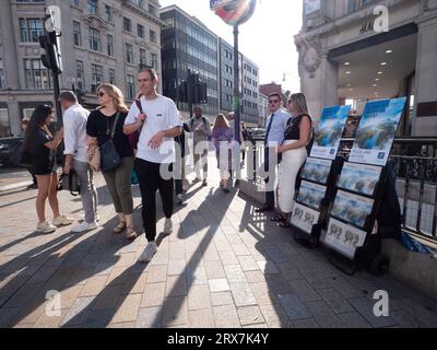 Jehovahs Zeugenstand im Oxford Circus, London, Großbritannien, mit Käufern, die an H&M Hennes und Mauritz Store vorbeigehen Stockfoto