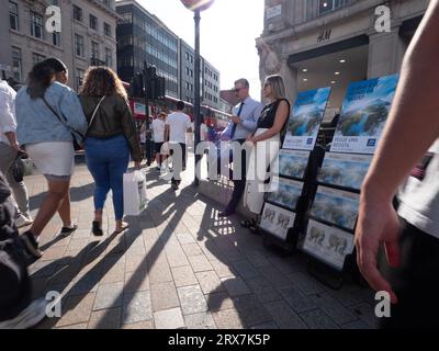 Jehovahs Zeugenstand im Oxford Circus, London, Großbritannien, mit Käufern, die an H&M Hennes und Mauritz Store vorbeigehen Stockfoto