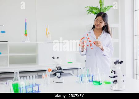 Porträt kluges junges asiatisches Teen-Wissenschaftlermädchen auf weißem Mantel, das im Chemiewissenschaftslabor der Schule steht und ein glückliches Lächeln hat Stockfoto
