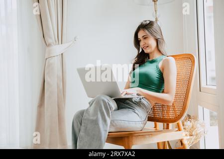 Junge Frau glücklich lächelnd Tippen auf Laptop-Computer Entspannen Sie sich im Wohnzimmer zu Hause. Menschen in der Freizeit mit modernen technischen Geräten Stockfoto