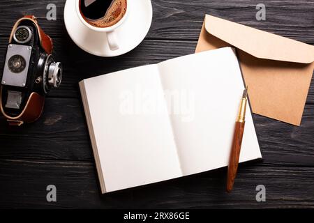 Ein offenes Buch, eine schöne Kamera mit Kaffee und ein Stift auf schwarzem Holzhintergrund mit einem Platz für eine Inschrift. Hochwertige Fotos Stockfoto