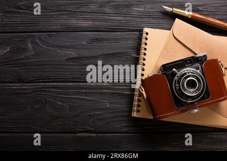 Ein Umschlag, eine schöne Kamera und ein Notizbuch mit einem Stift auf einem schwarzen Holzhintergrund mit einem Platz für eine Beschriftung. Hochwertige Fotos Stockfoto