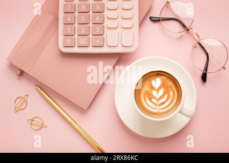 Taschenrechner, eine Tasse Kaffee mit schönem Muster und einem Notizblock auf rosafarbenem Hintergrund. Für Text platzieren. Hochwertige Fotos Stockfoto