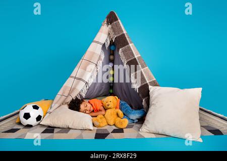 Foto des kleinen niedlichen Jungen, der im selbstgemachten Zelt schläft, isolierter blauer Farbhintergrund Stockfoto