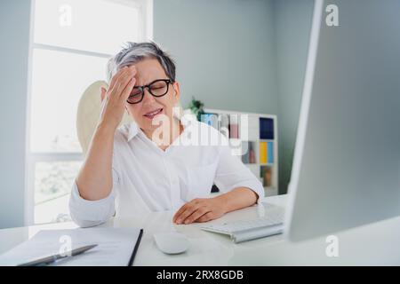 Foto einer überarbeiteten traurigen Sekretärin trägt weißes Hemd und spürt Kopfschmerz beim Arbeiten mit modernen Geräten in der Arbeitswerkstatt Stockfoto