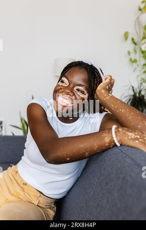 Fröhliche junge Erwachsene schwarze Frau, die tagträumt und sich zu Hause auf dem Sofa entspannt. Stockfoto