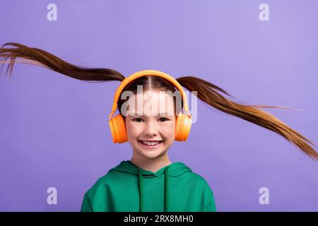 Foto von fröhlich funky kleines Mädchen gekleidet grünen Hoody genießen Musik fliegenden Pferdeschwanz isoliert lila Farbe Hintergrund Stockfoto