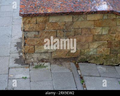 Sandsteinwand, Hintergrund der Dekoration. Die Verkleidung aus Steingut ist von der Fassade des Gebäudes gefallen. Braune Wand aus Rohstein, Hintergrund, Stockfoto