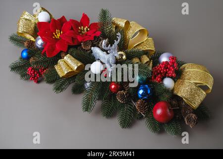 Dekorative Weihnachtskomposition aus Tannenzweigen für Tisch oder Kamin. Rentierspielzeug und goldene Bänder mit Bobbles und Beeren Stockfoto