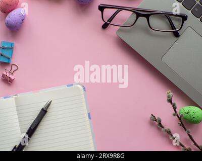 Osterarbeitskonzept. Flach liegend. Business-Schreibtisch mit Geräten und bunten ostereiern auf rosafarbenem Hintergrund. Federdekoration Arbeitsgerät Stockfoto