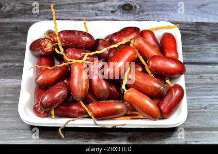 Zaghloul ägyptische rote Datteln wachsen um die Dutzenden an langen gelben Stämmen, botanisch als Phoenix dactylifera klassifiziert und sind die Frucht der Dattelpalme Stockfoto