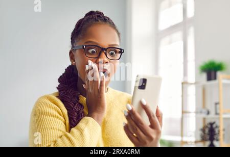 Frau ist erstaunt über Inhalte, die sie gesehen hat oder die schockierende Nachricht auf dem Bildschirm des Mobiltelefons liest. Stockfoto