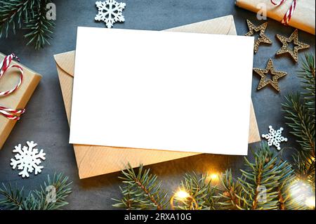 Leere weiße Papierkarte mit braunem Umschlag, Weihnachtskiefer und handgefertigter Geschenkbox auf grauem Hintergrund. Weihnachtskonzept. Stockfoto