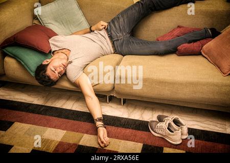 Foto eines jungen und gutaussehenden Mannes, der in einer seltsamen Position auf dem Boden mit einem Kissen unter dem Kopf ruht, vielleicht betrunken oder sehr müde Stockfoto
