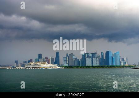 Blick von der Straße von Singapur auf die Skyline von Singapur unter stürmischem Himmel mit dem Marina Bay Cruise Centre im Vordergrund. Singapur . Stockfoto