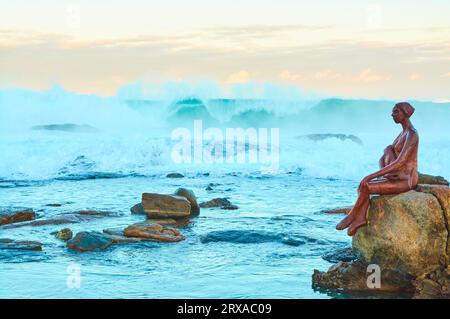 Eine Skulptur namens Layla des Künstlers Russell Sheridan in der Nähe der Margaret River Mouth am Prevelly Beach bei Sonnenaufgang mit brechender Welle, Western Australia. Stockfoto