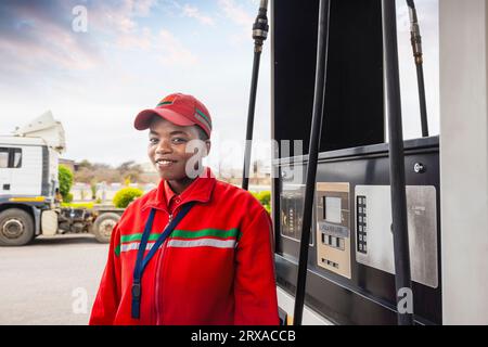 afroamerikanerin in roter Uniform an der Gaspumpe, LKW im Hintergrund Stockfoto