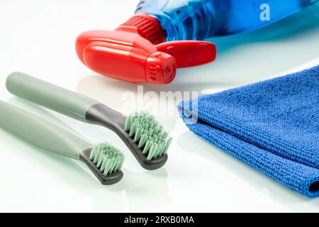 Reinigungszubehör. Bürsten, blaue Serviette und Flasche mit Reinigungsflüssigkeit auf weißem Hintergrund Stockfoto