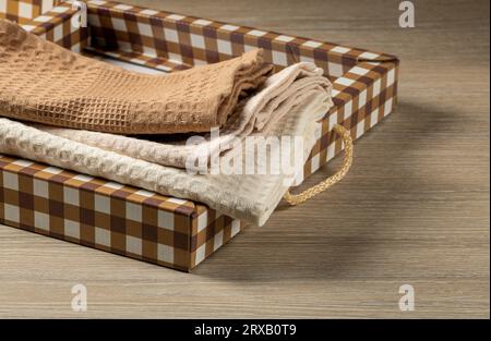 Waffelhandtücher werden in einer karierten Geschenkbox auf einem Holztisch gestapelt, mit Blick von oben, Hausleben Stockfoto