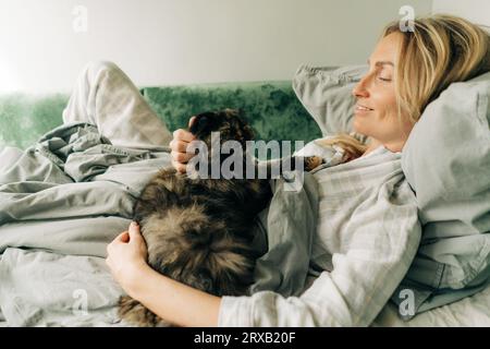 Eine junge Frau liegt im Bett und streichelt eine Hauskatze. Stockfoto