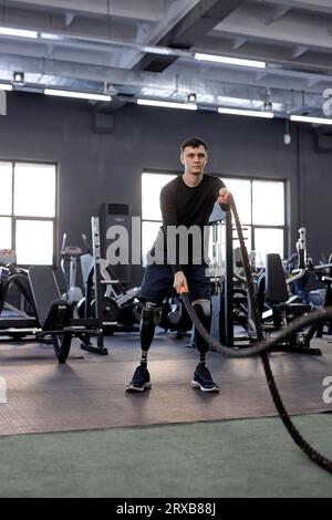 Motivierter, starker, muskulöser junger Sportler mit künstlichem Beintraining mit Seilen im Fitnessstudio, Vollbild, Lifestyle, Freizeit, Freizeit Stockfoto