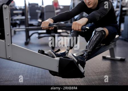 Behinderte Person nutzt eine Rudermaschine im Sportcenter, beschnittene Schuss, Fokus auf künstliche Beine Lebensstil Gesundheit und Körperpflege Stockfoto